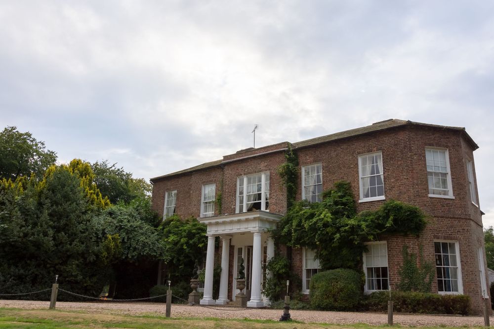 A stately brick Georgian-style mansion with white columns and climbing vines on its facade.