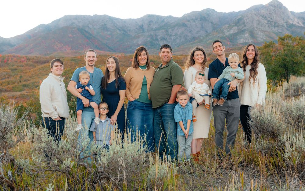 Large family posing together in a field with colorful autumn mountains in the background. Megan Snell Photo Utah Weddings