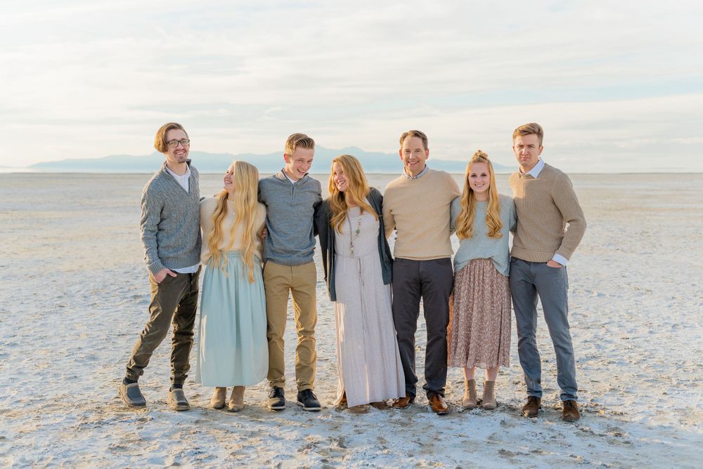 Family of six smiling together on a salt flat with mountains in the background during an outdoor photo session.