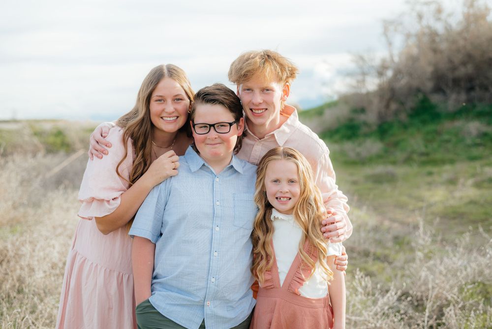 Four siblings embrace and smile together in an outdoor field setting.