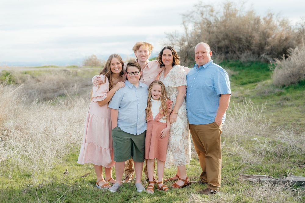 Happy family of six poses outdoors in a grassy field with soft natural light.