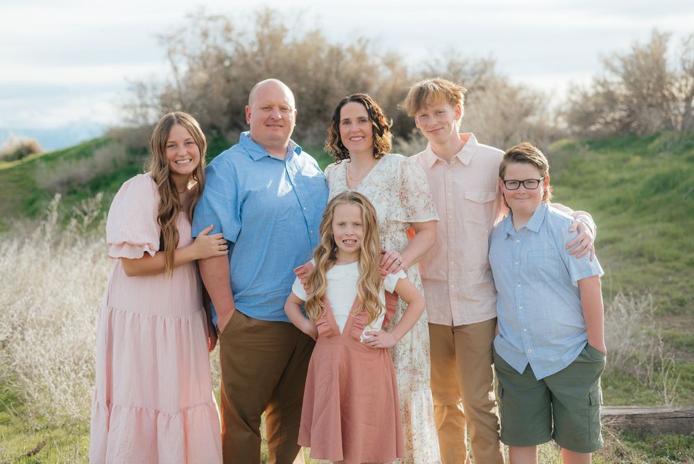 Family of six poses together on a scenic hillside trail in pastel outfits.