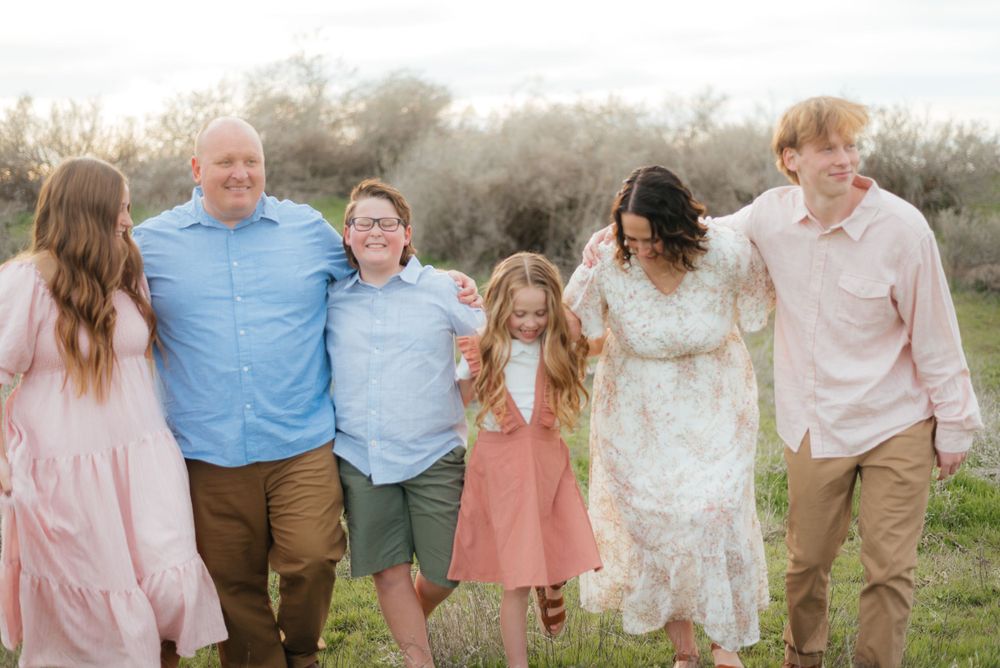 Family of six walks joyfully together through a scenic green meadow.