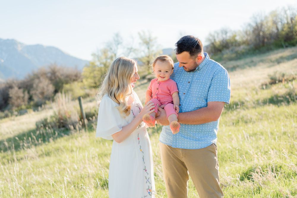 Happy young family with a baby girl enjoying a sunny day in a green mountain meadow.