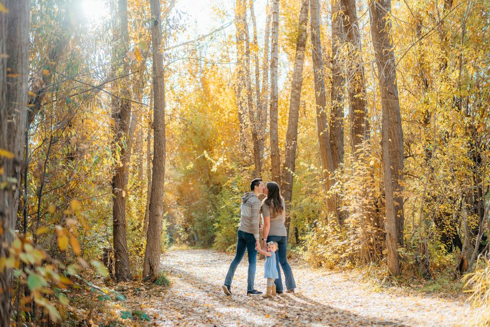 Couple kissing on a sunlit forest path surrounded by vibrant golden autumn foliage. Megan Snell Photo Utah Weddings