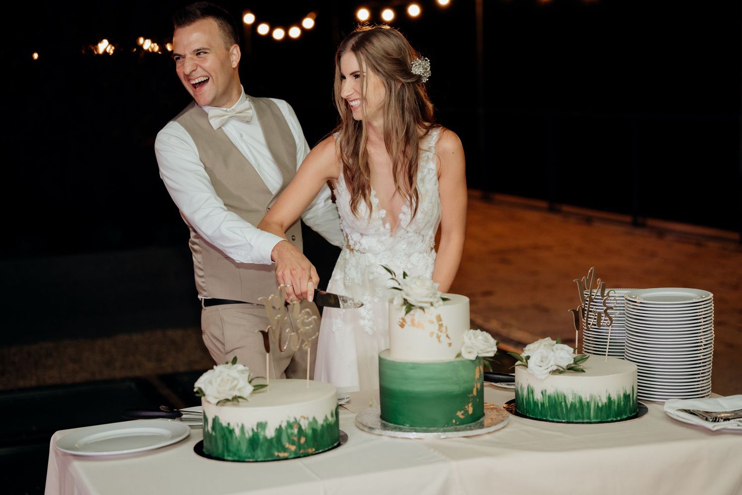 A couple cuts their green ombre wedding cake display at an outdoor evening reception.