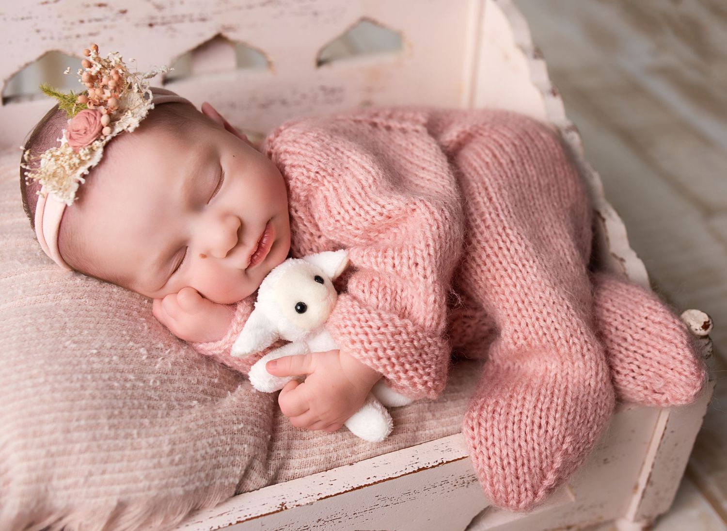 Newborn baby girl in pink knit romper sleeping while holding a white stuffed bunny toy.