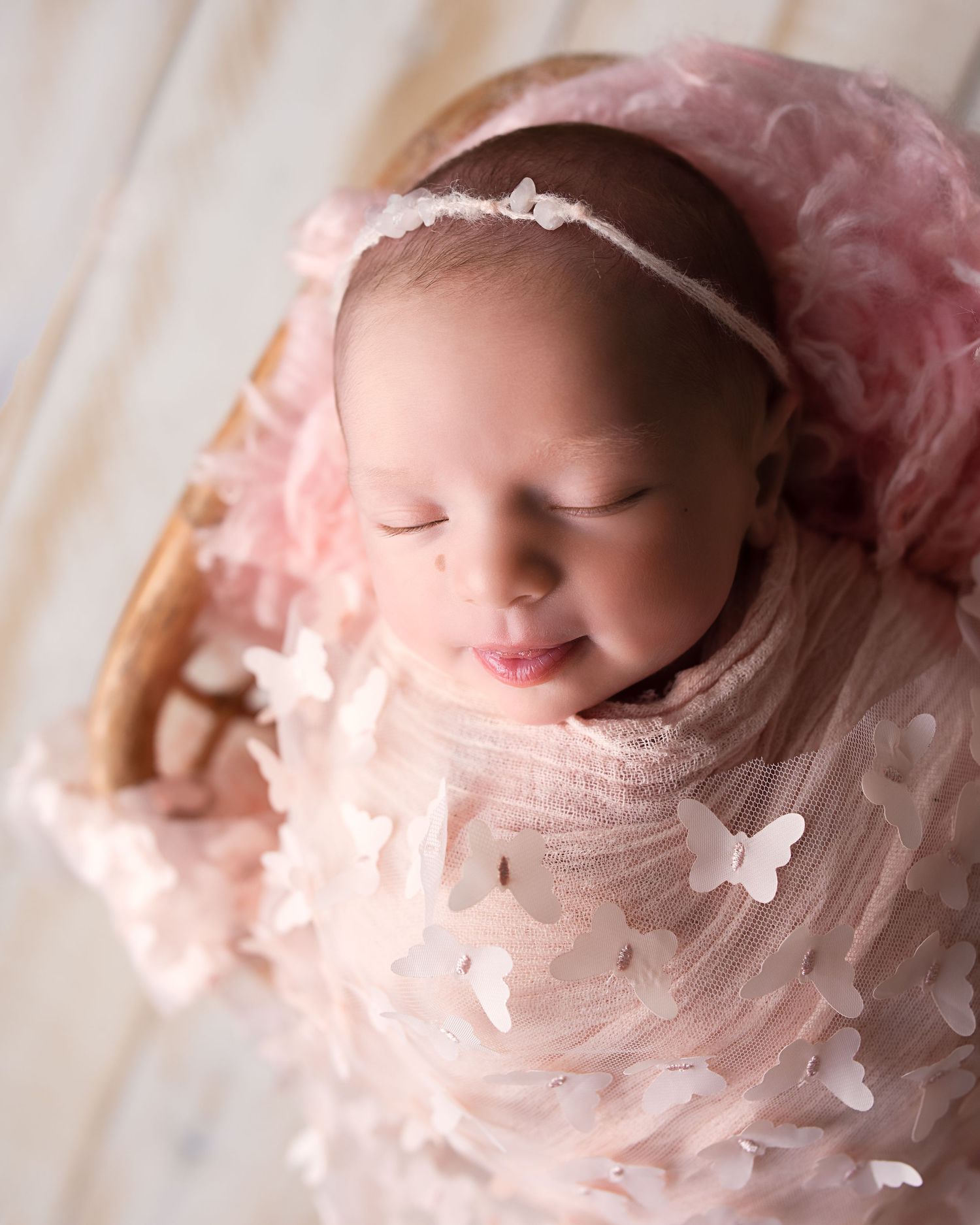 Sleeping newborn baby girl in pink butterfly wrap with floral headband in a wicker basket.