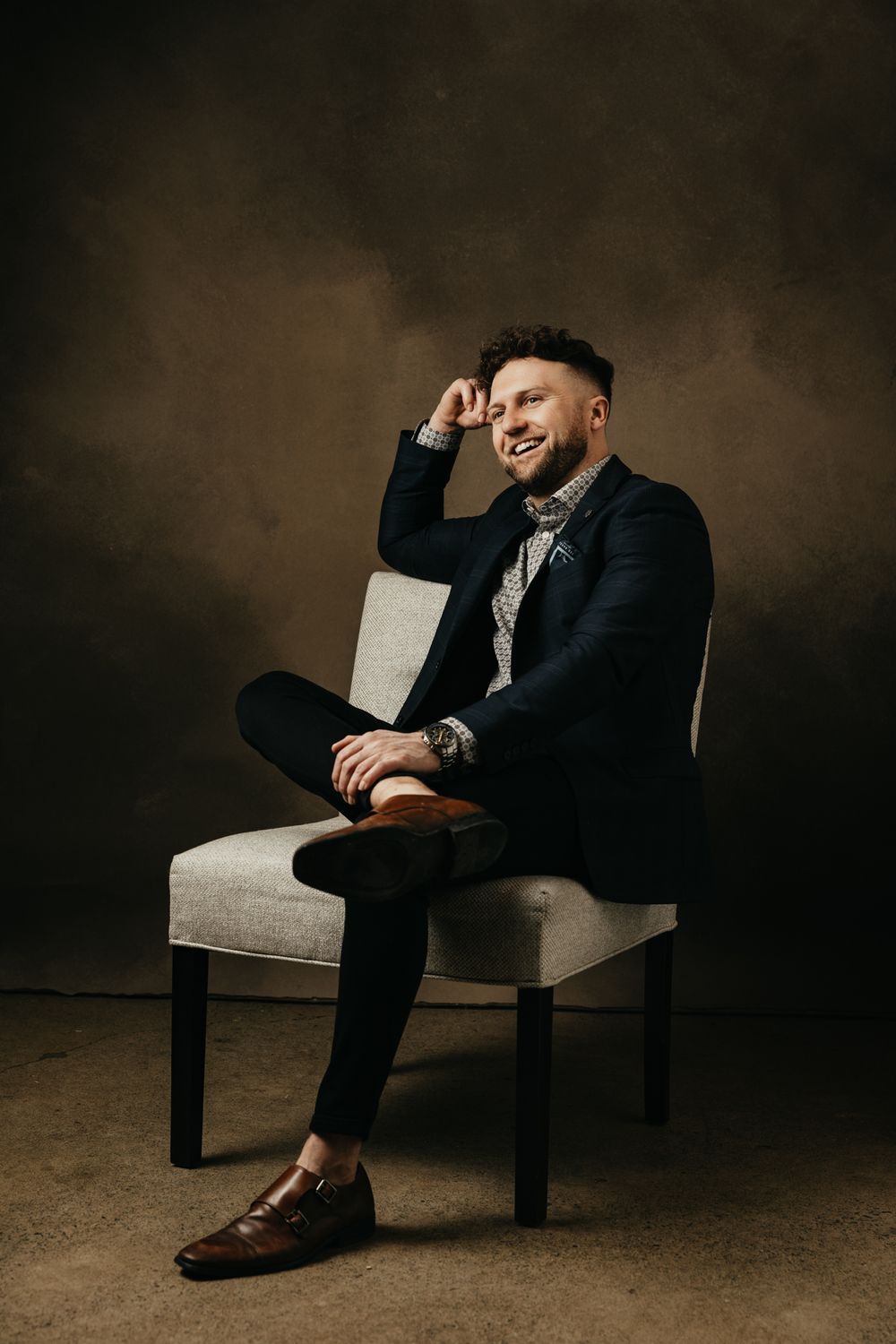 Artistic portrait series showing relaxed poses on modern chair against dark background.