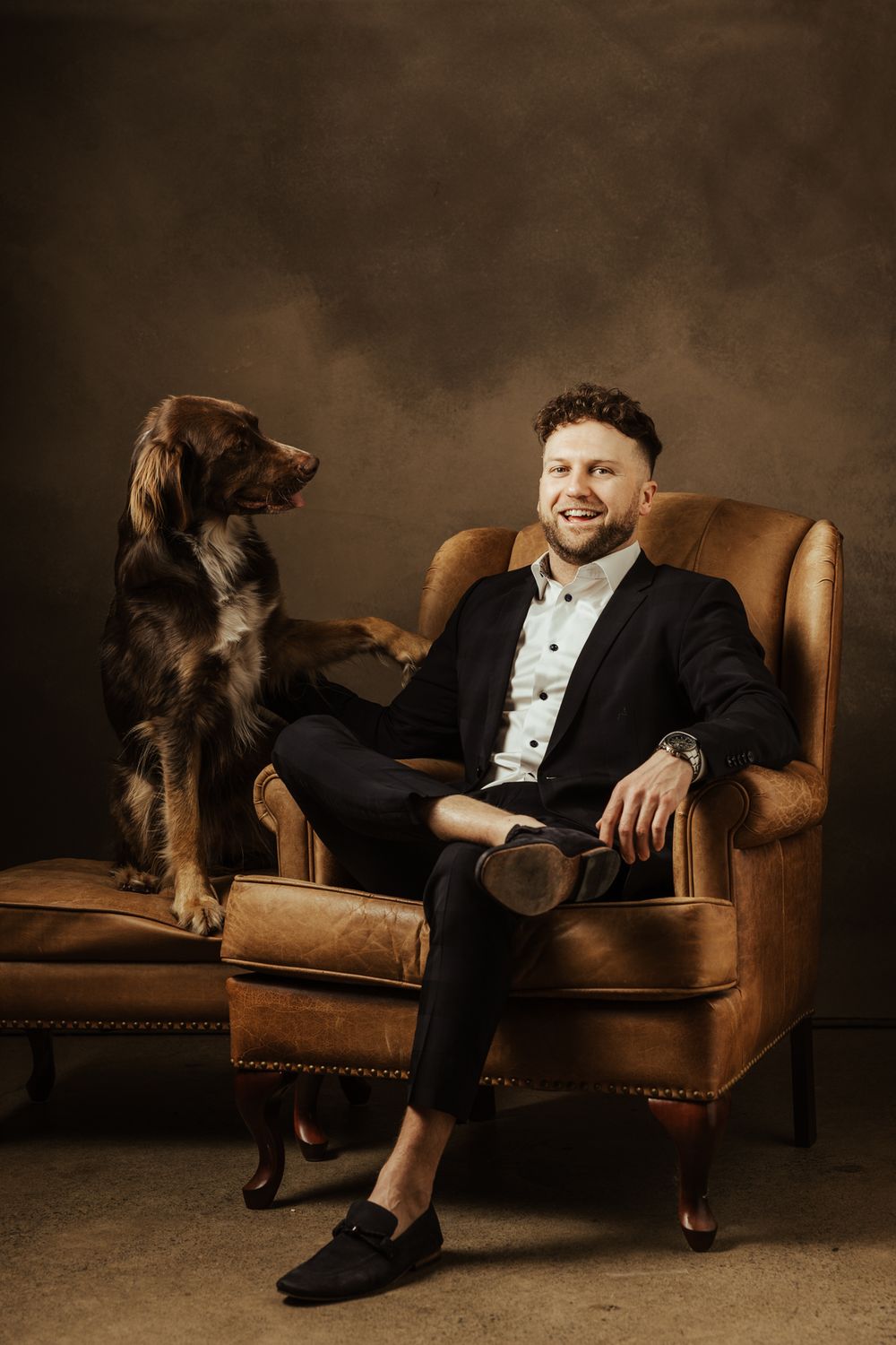 Studio photoshoot featuring a person and dog relaxing on vintage leather furniture.