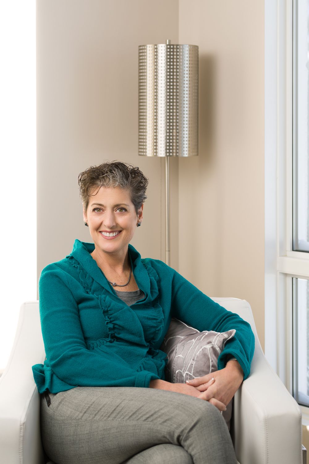 Casual portrait of person in teal sweater sitting relaxed in white armchair.