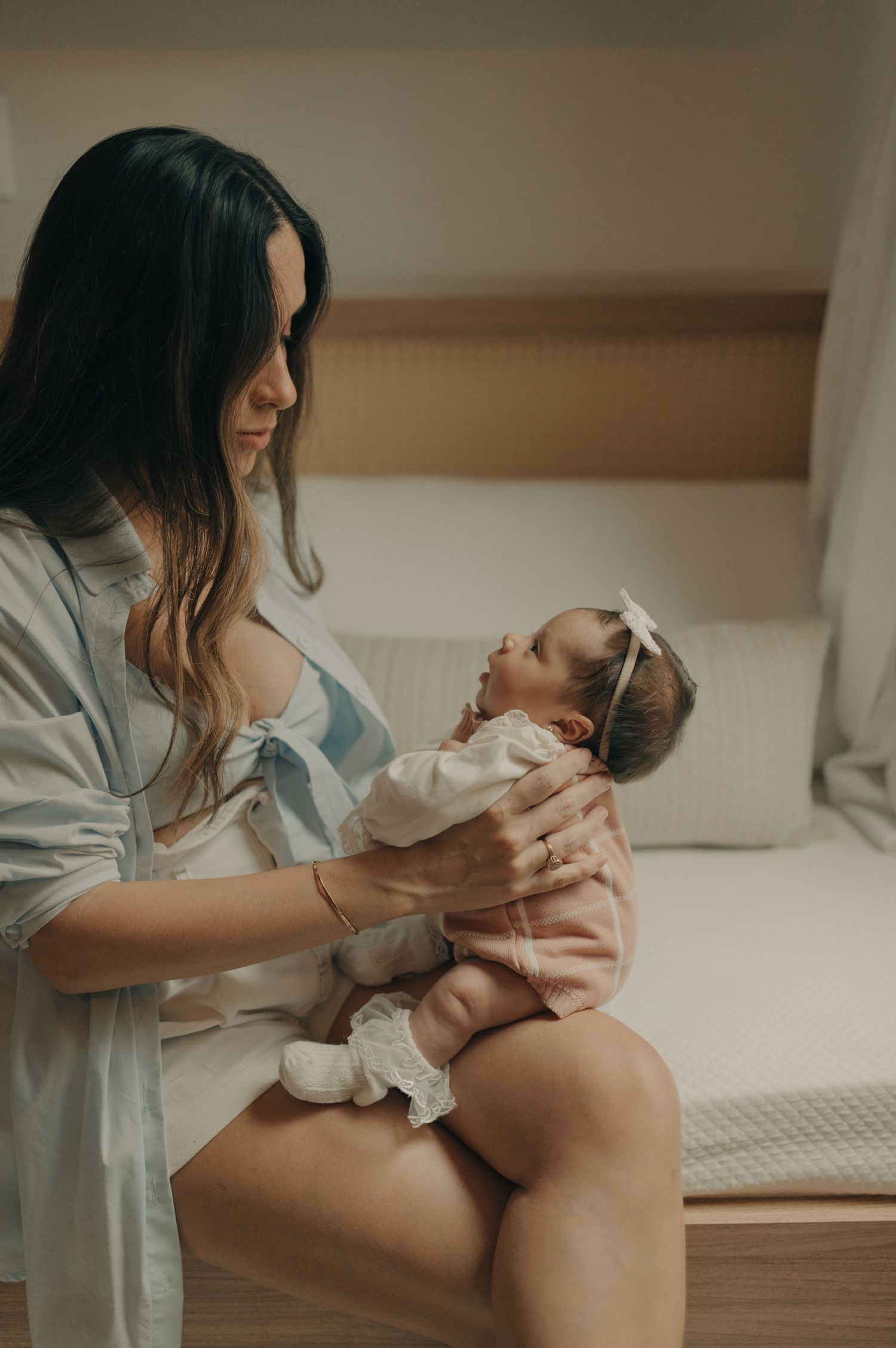 Candid lifestyle photo of parent and infant interacting on bed in natural light.