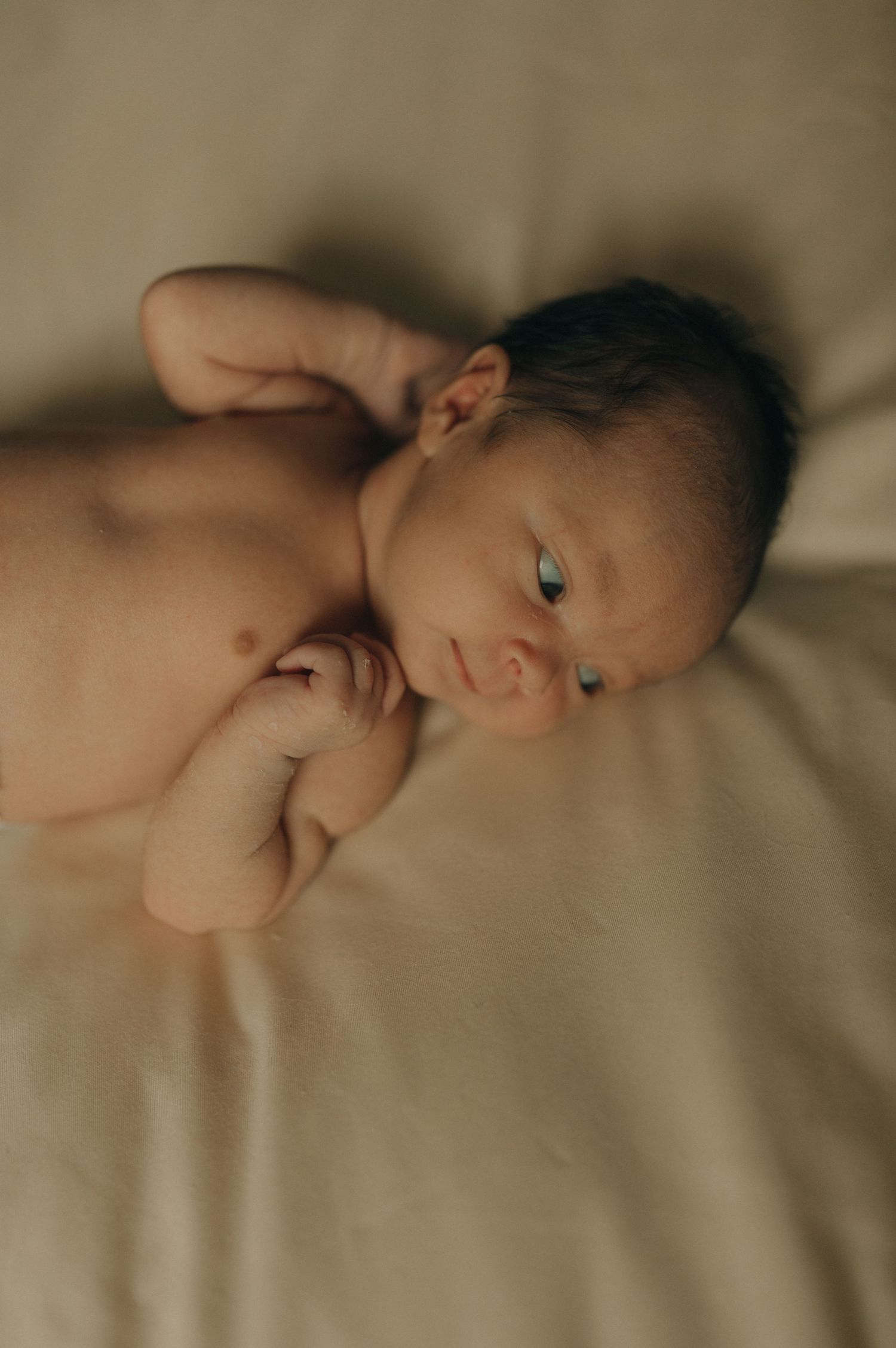 Close up portrait of a newborn baby lying on beige bedding with bright alert eyes.