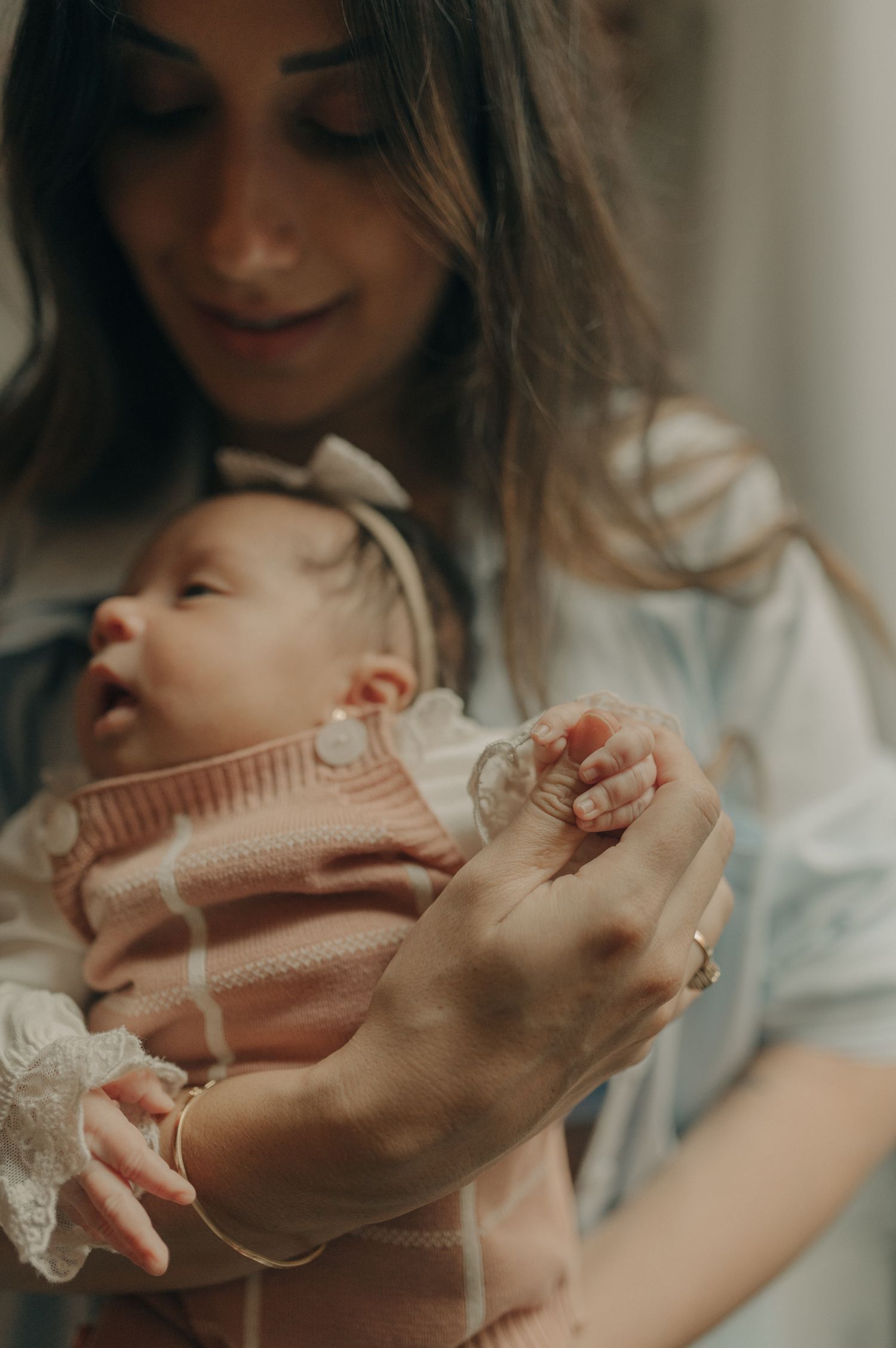 An infant in a pink sweater being tenderly cradled in loving arms.