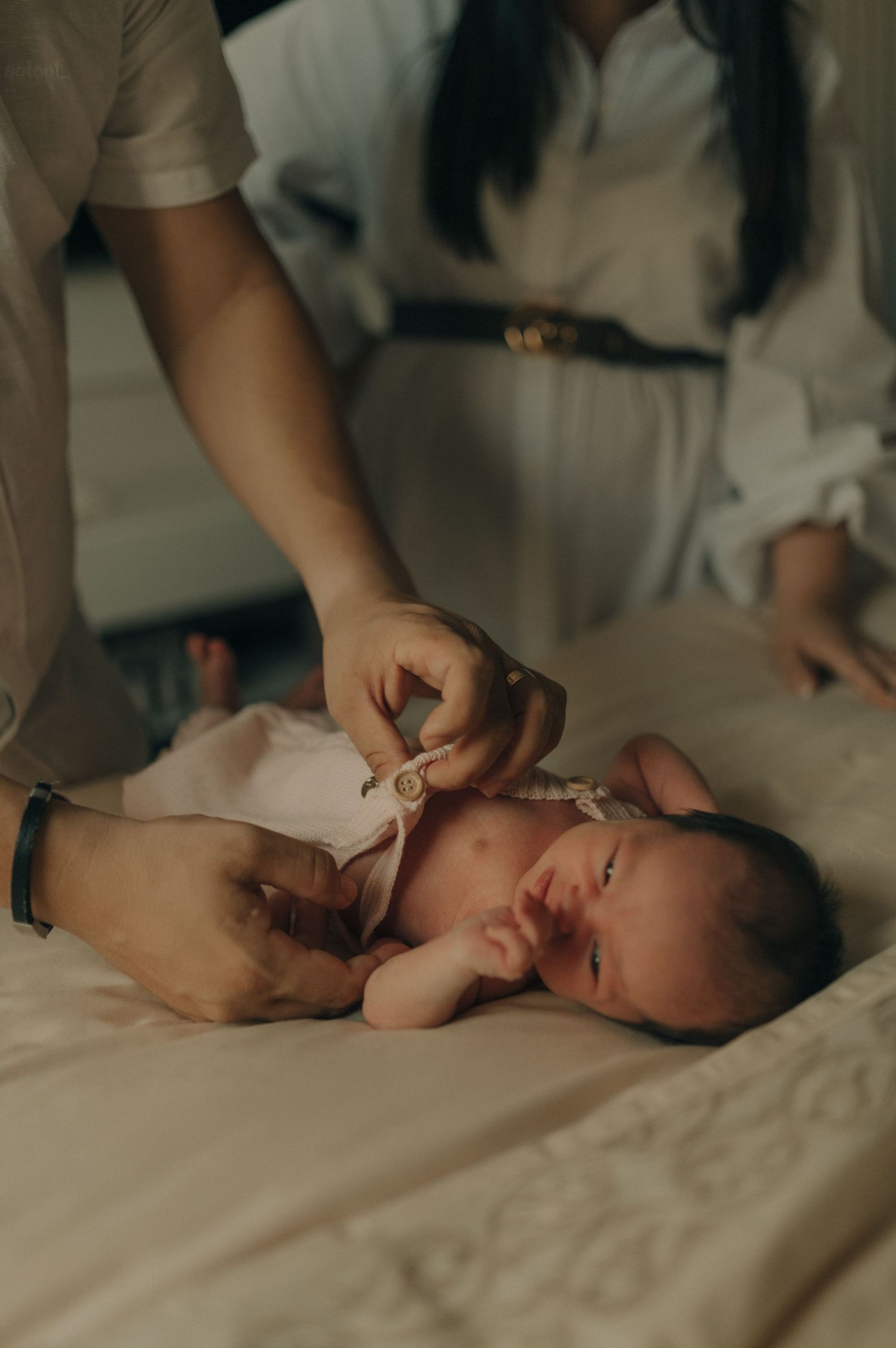 A delicate moment during newborn care on soft white bedding.