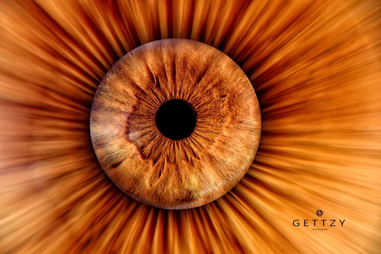 Extreme macro photograph of an amber colored human iris with radiating patterns and a dark pupil.