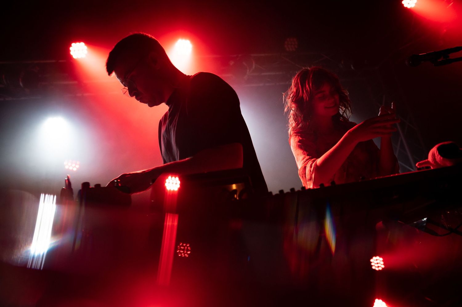Concert performers silhouetted in red and white stage lighting during live music performance.