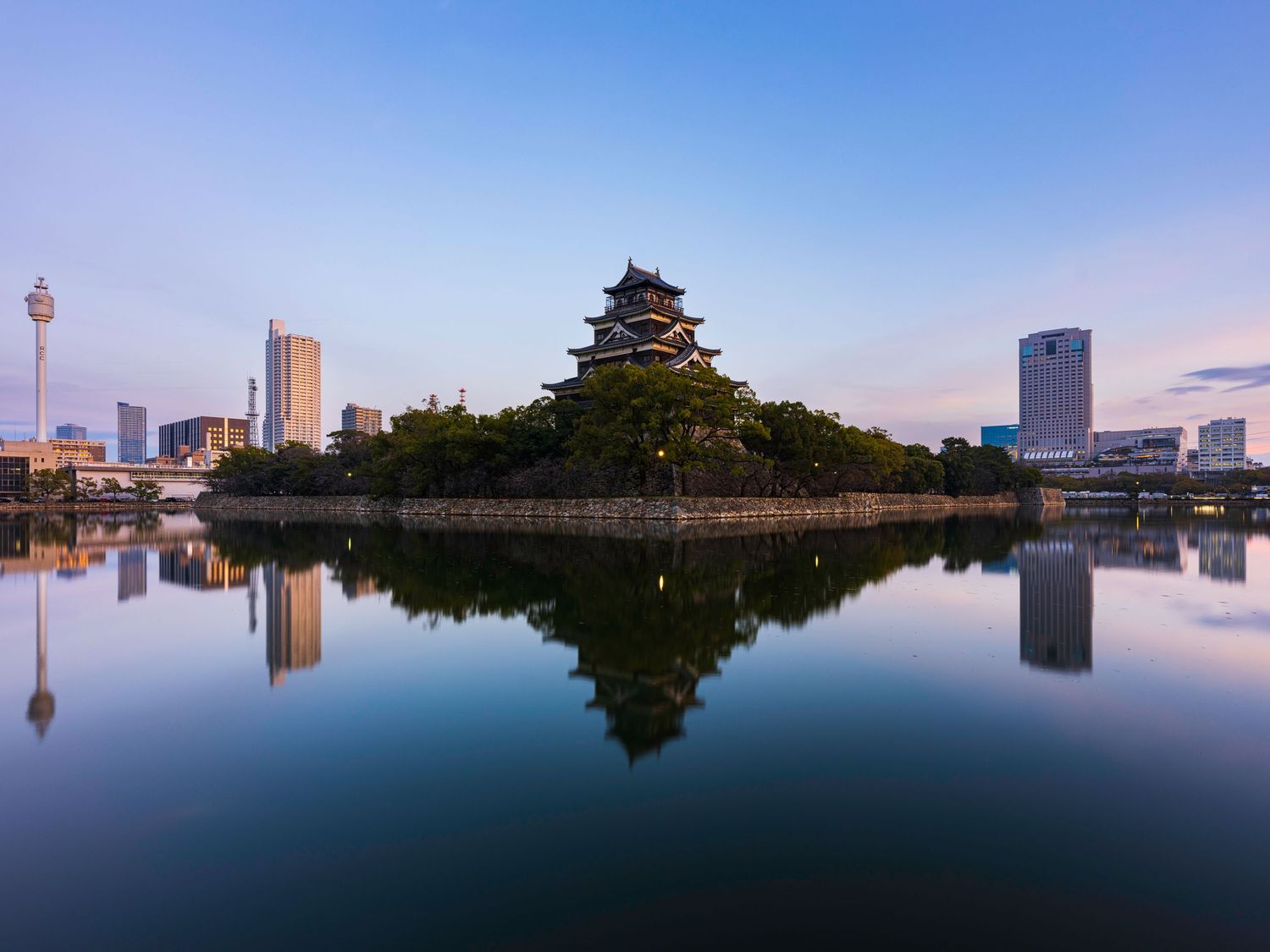 Panoramic cityscape reflection in still waters with Japanese architecture and mountain backdrop.