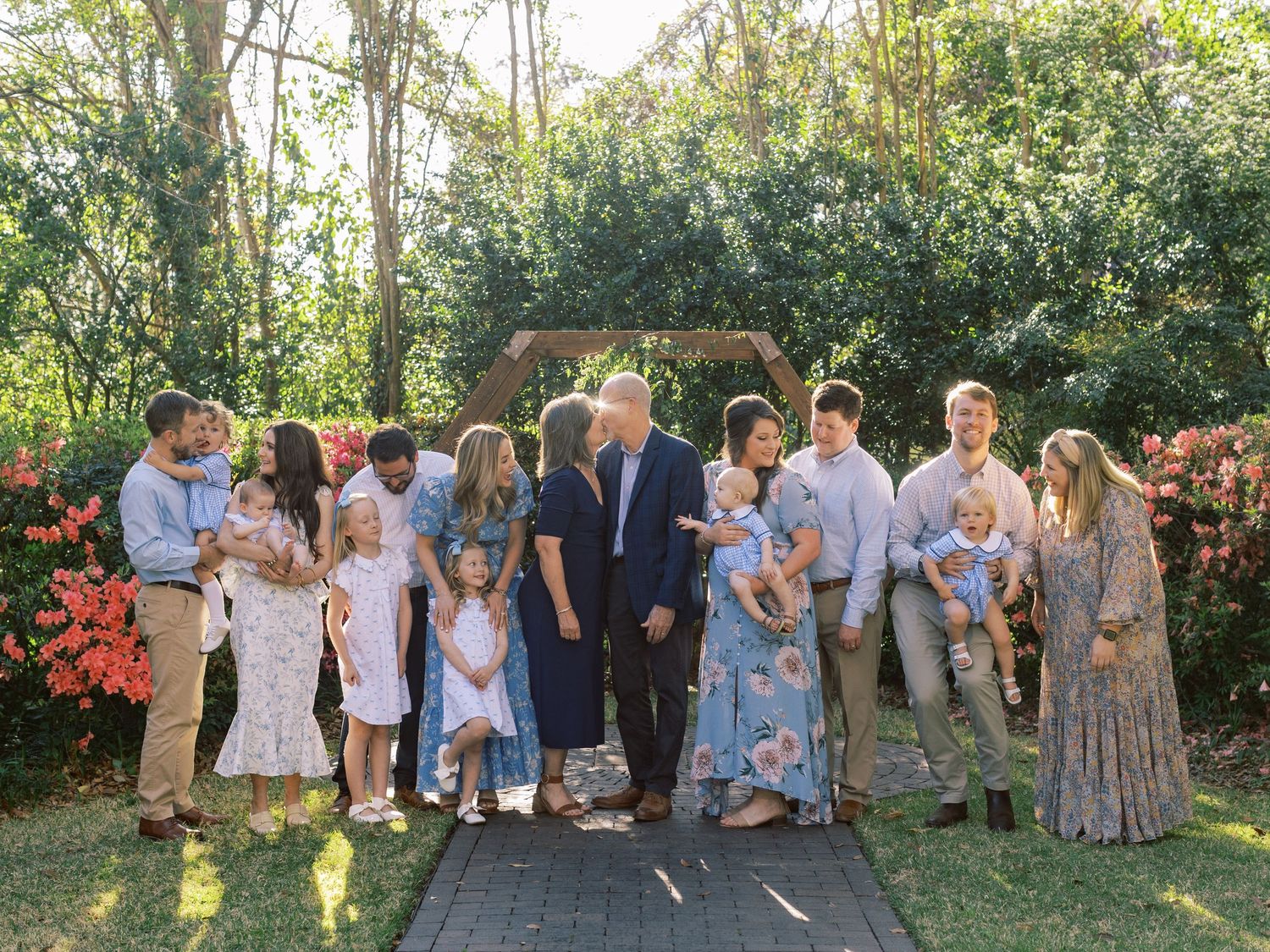 Extended family gathering outdoors for a formal group photo in a garden setting with blooming flowers.