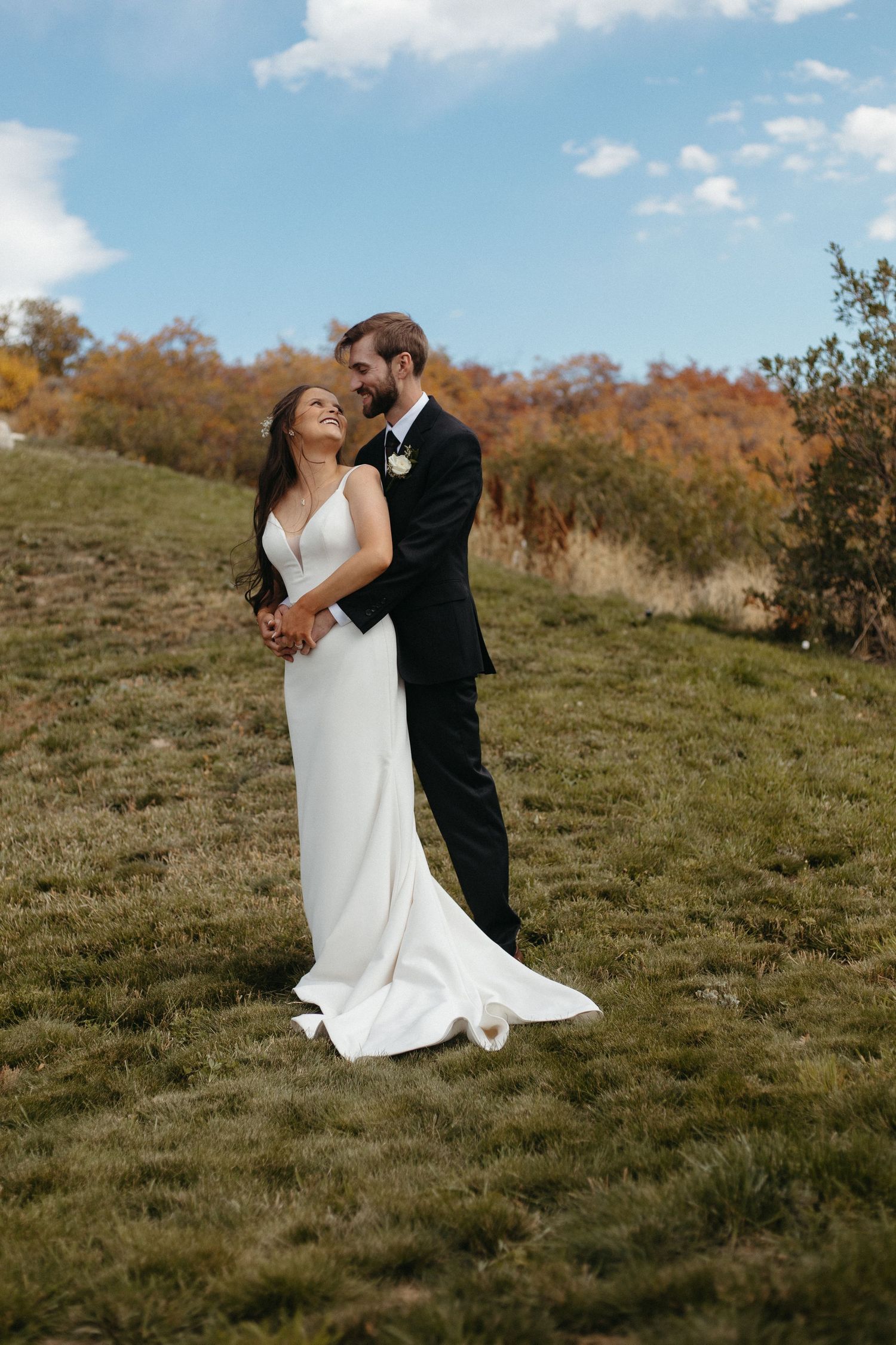 A couple shares an intimate moment on a grassy hillside during their wedding day.