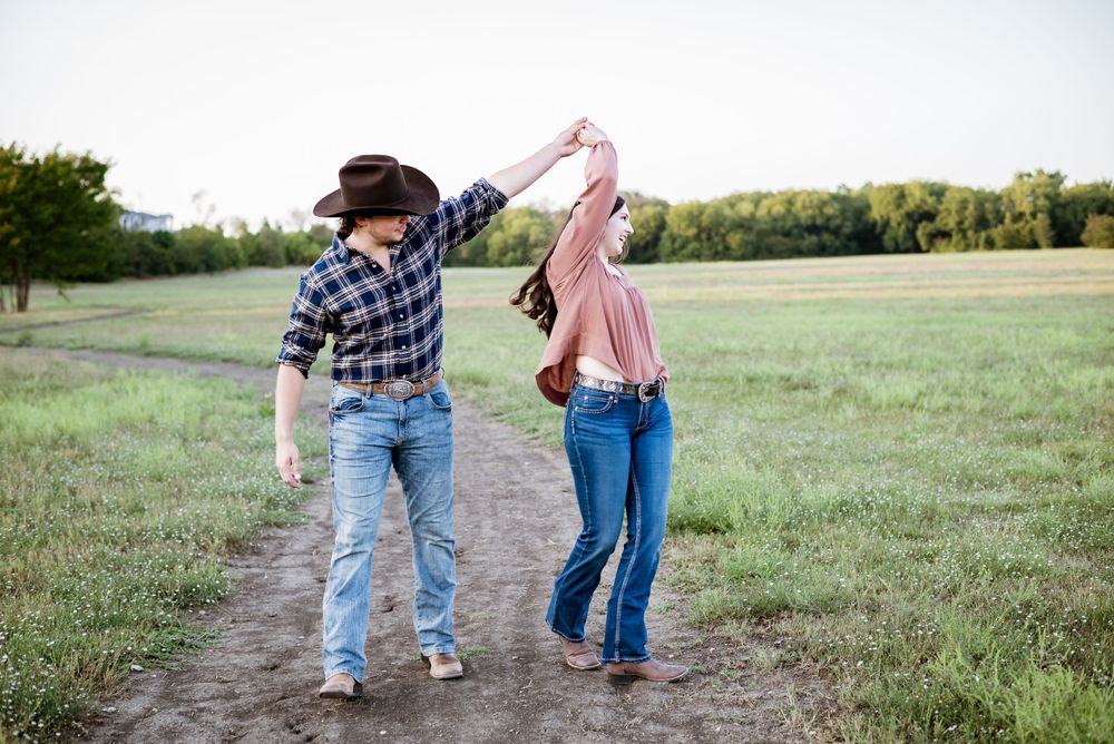 Couple dancing on dirt path through countryside field.
