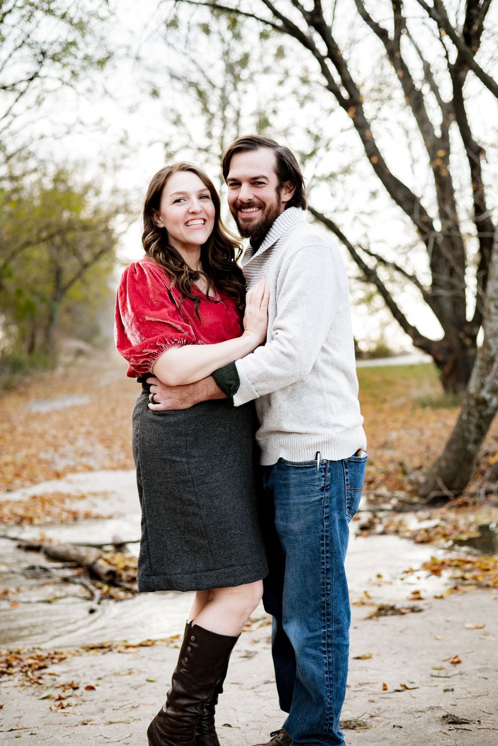A couple embraces while smiling and laughing together on an autumn day.