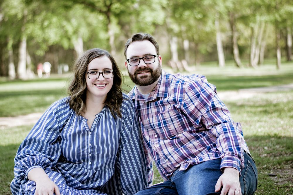 Couple in plaid and stripes sitting together outdoors in park setting.