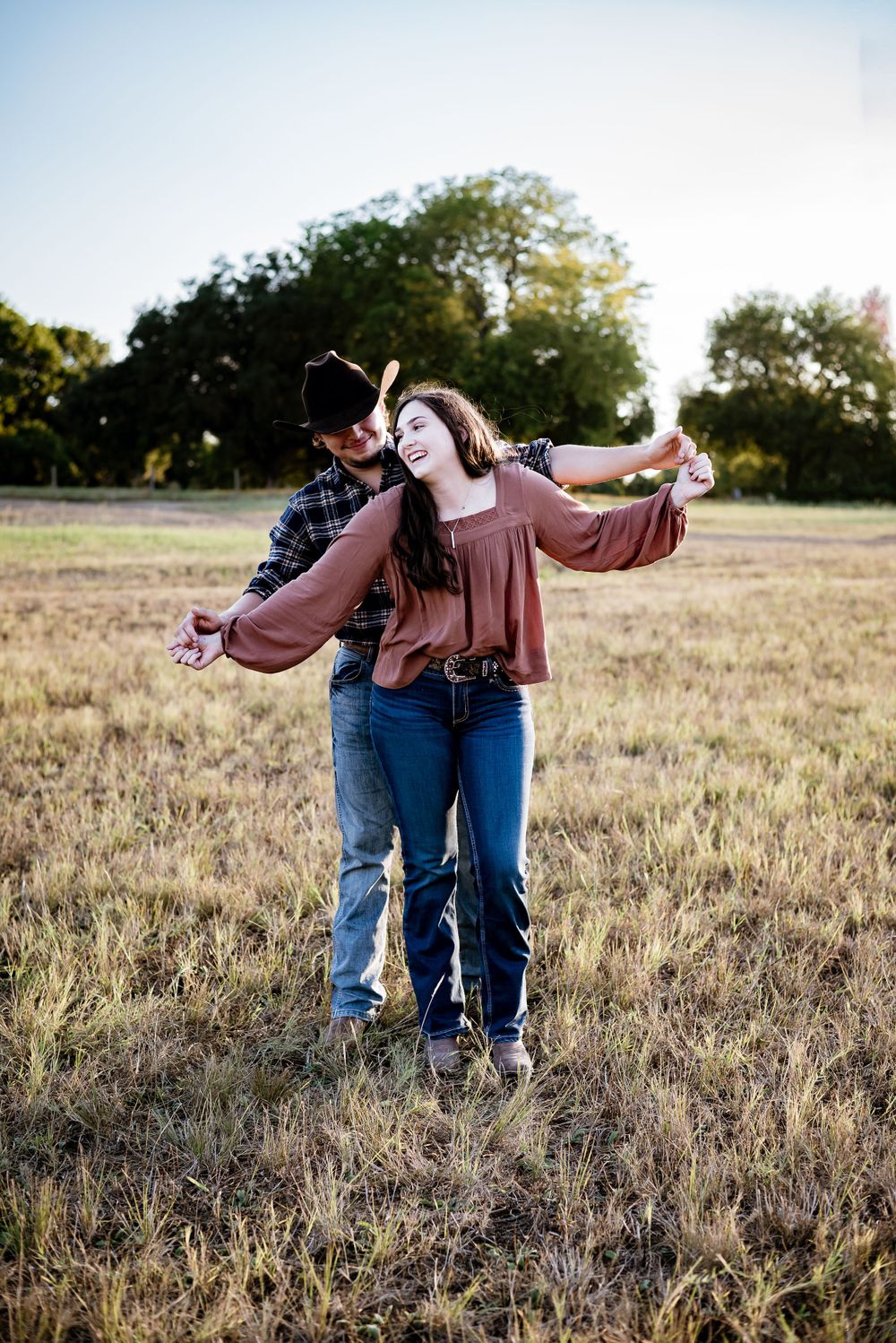 Couple dancing and laughing together in rustic field at dusk.