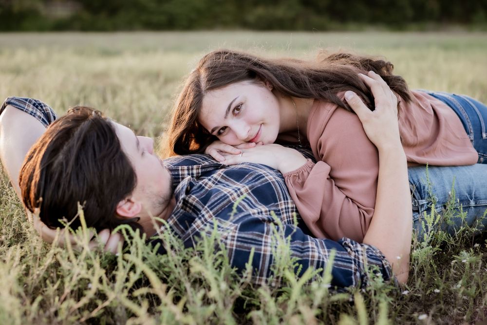 Couple lying in tall grass field sharing intimate moment.