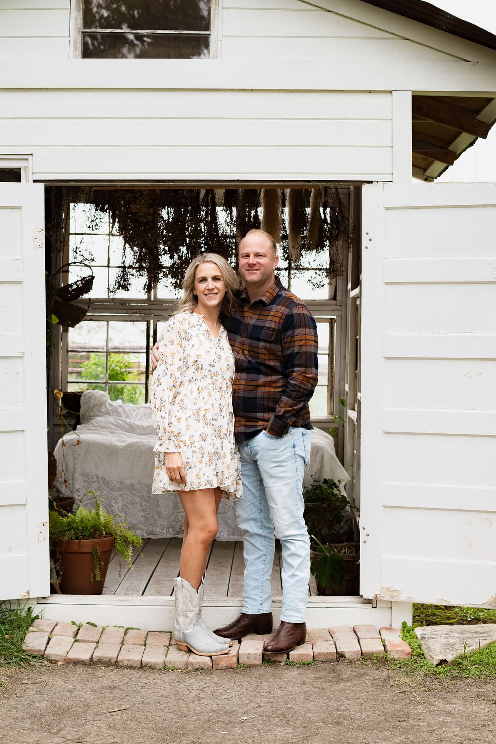 Couple standing in white farmhouse doorway wearing casual autumn attire.