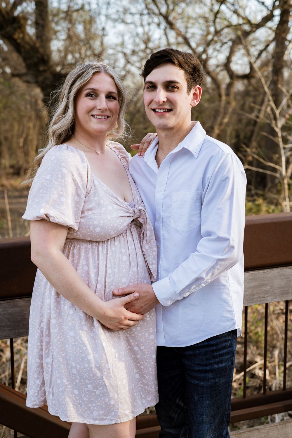Couple in pink dress and blue shirt embracing on wooden deck.