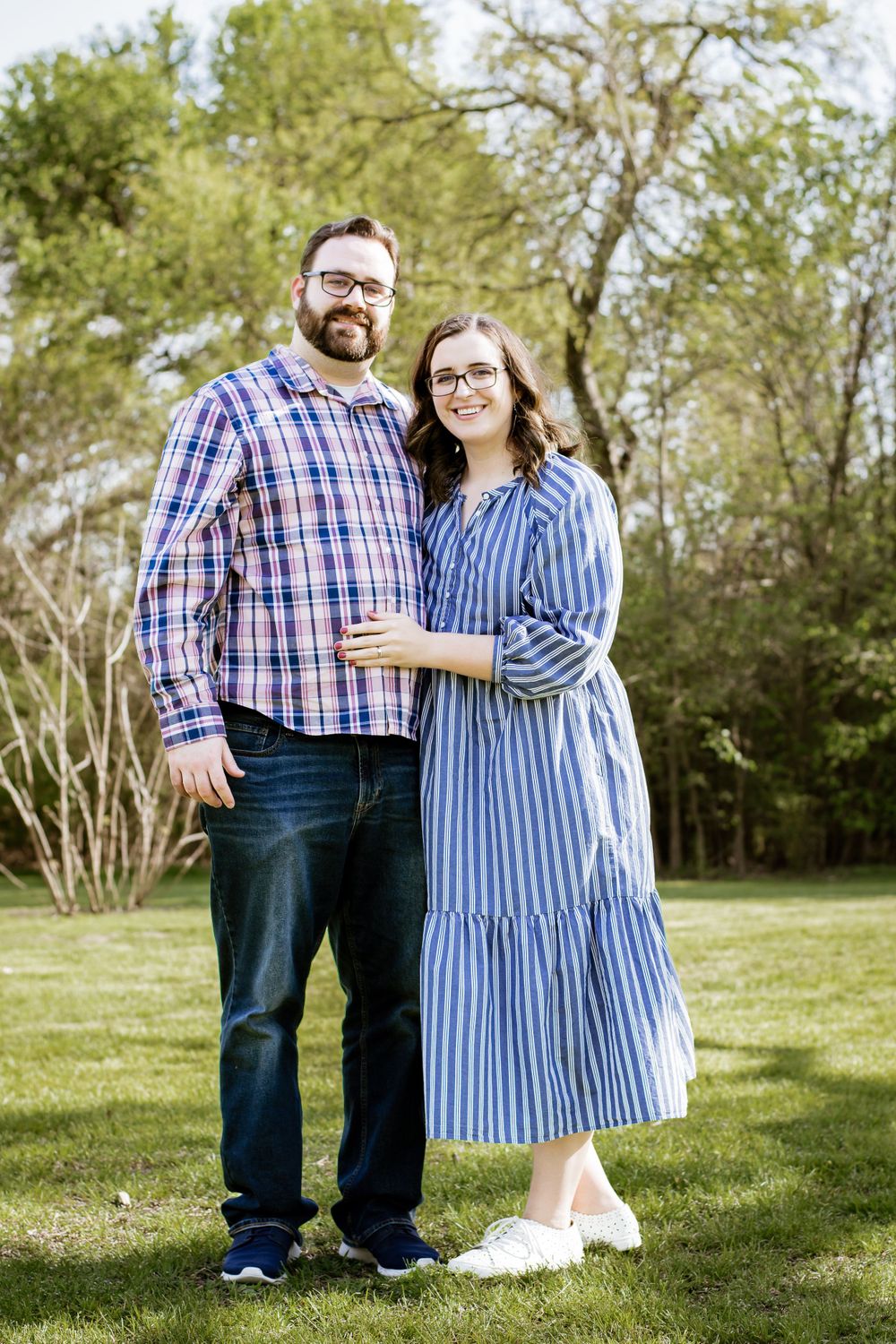 Couple in casual attire standing together on grass in spring setting.