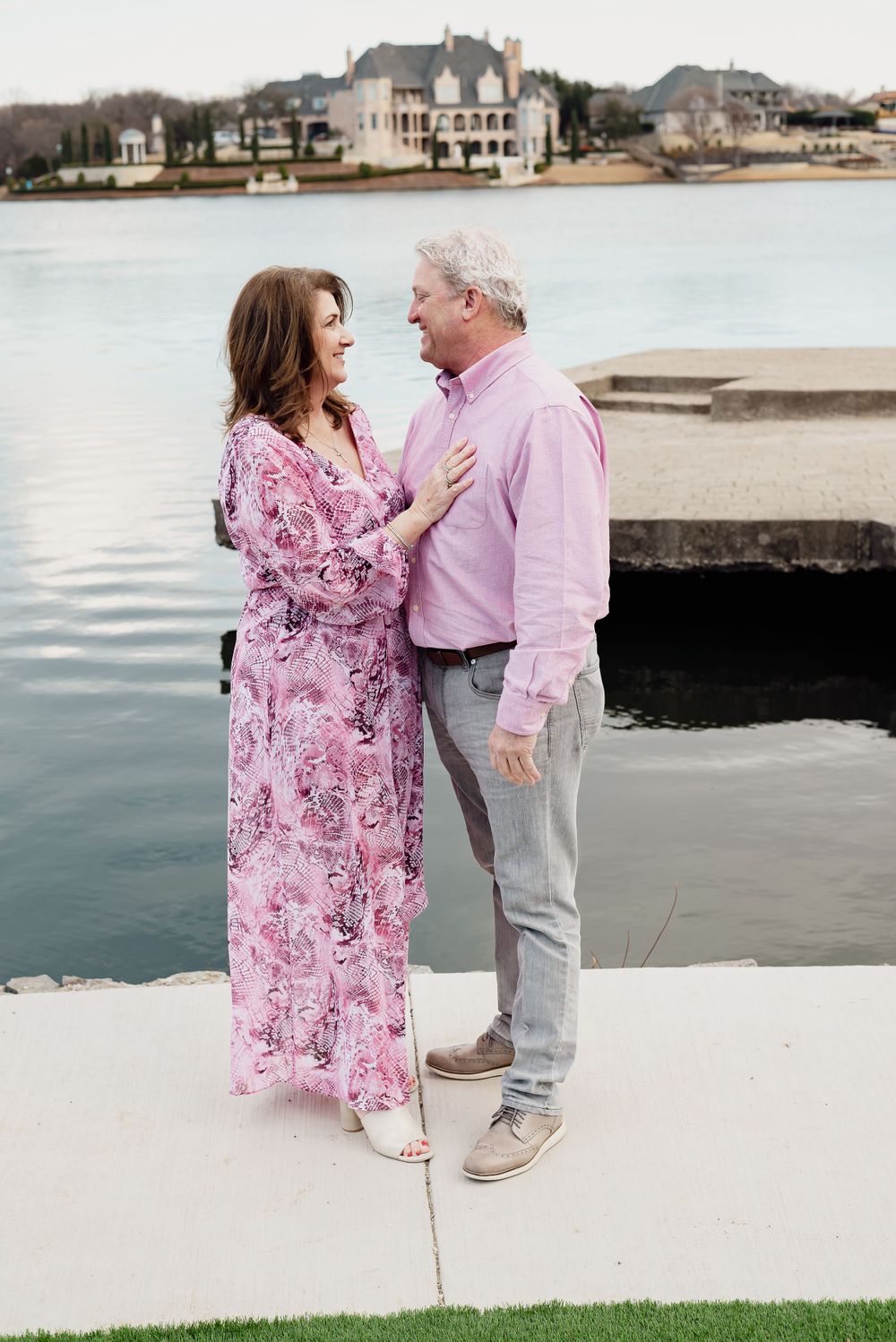 A couple shares a romantic moment by the waterfront with coastal homes in background.