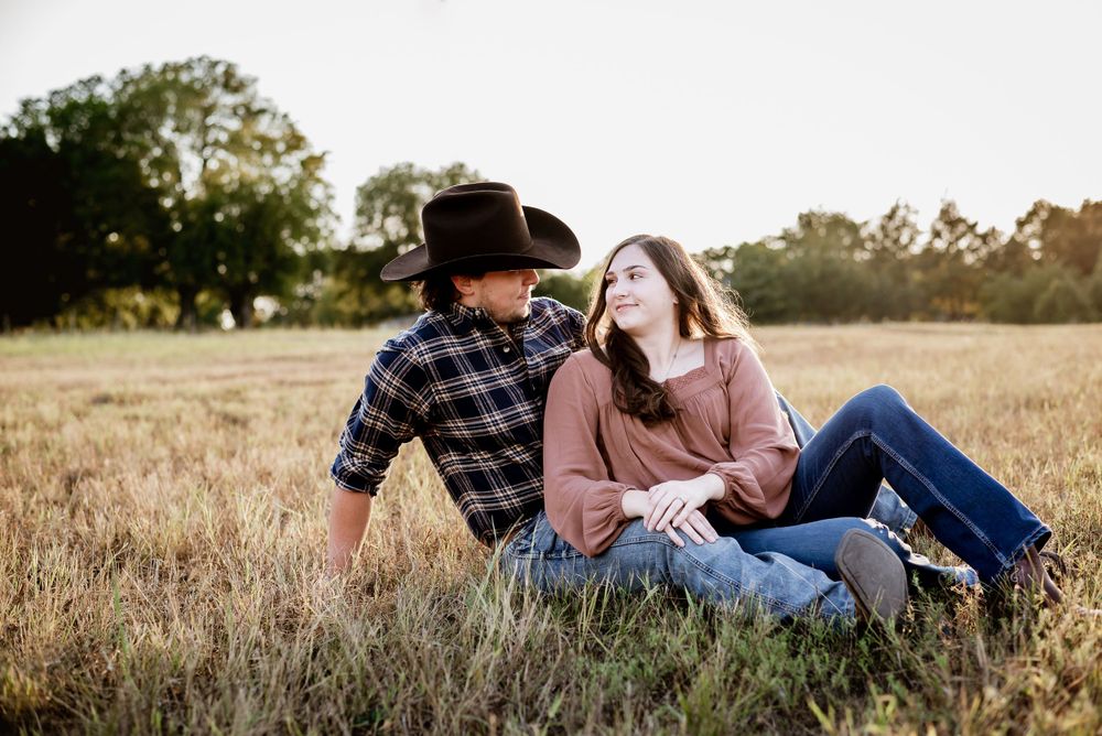 Couple sitting together laughing in golden field at sunset.