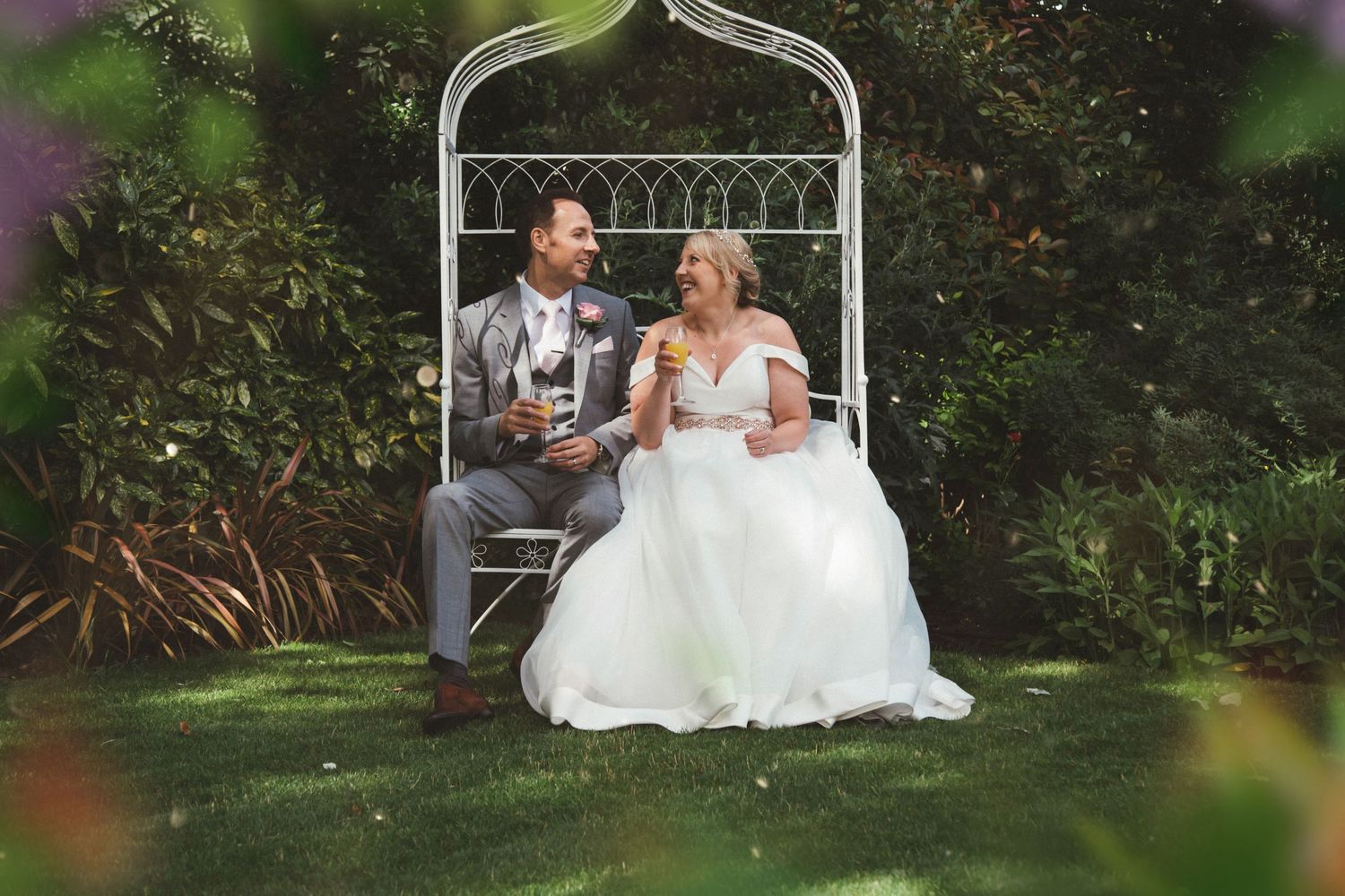 A newlywed couple shares intimate moments in a garden setting with white wedding attire.