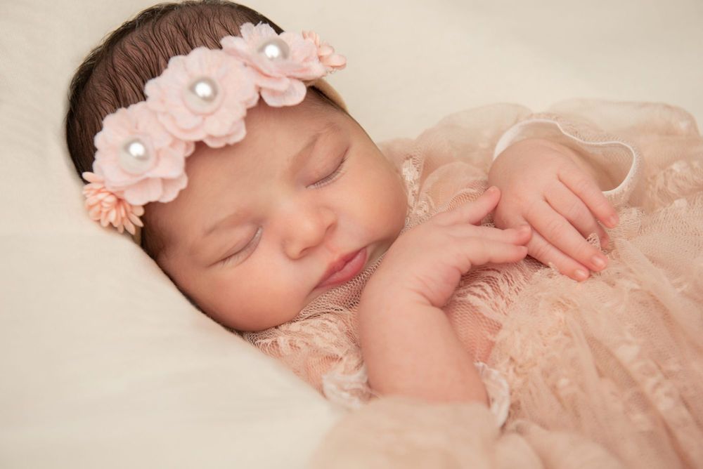 Peaceful sleeping newborn wearing delicate pink floral headband and lace wrap.