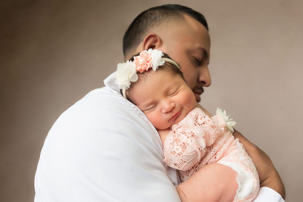 Sweet portrait of parent cradling sleeping baby in pink lace outfit.