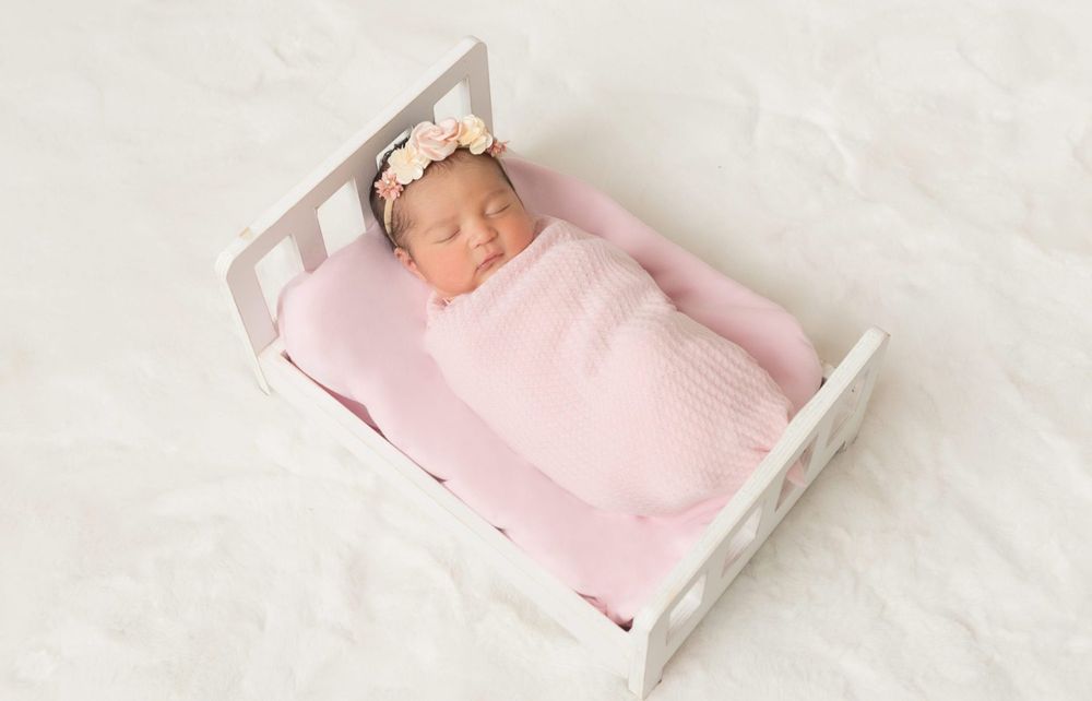 Peaceful sleeping newborn swaddled in pink blanket lying in white wooden bed.