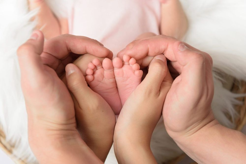 Adult and child hands gently cradling tiny newborn baby feet on white background.