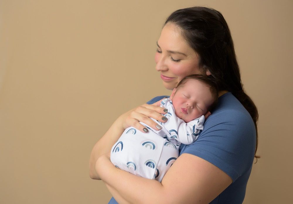 Tender moment as parent cradles sleeping newborn against neutral backdrop.