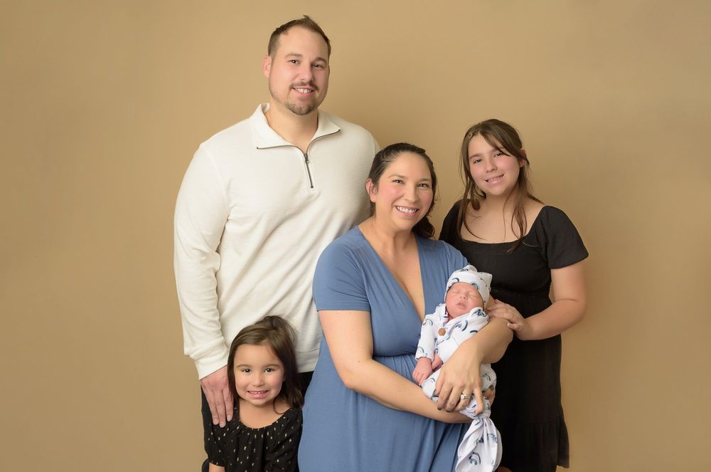 Family portrait with new baby against beige background in studio setting.