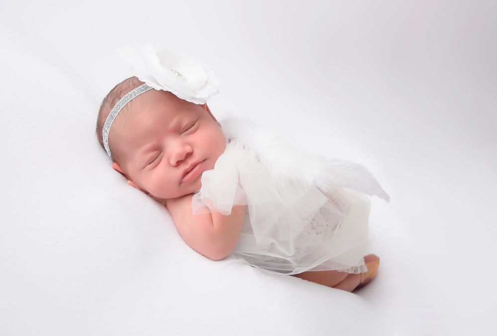 Sleeping newborn in white outfit and headband on light background.