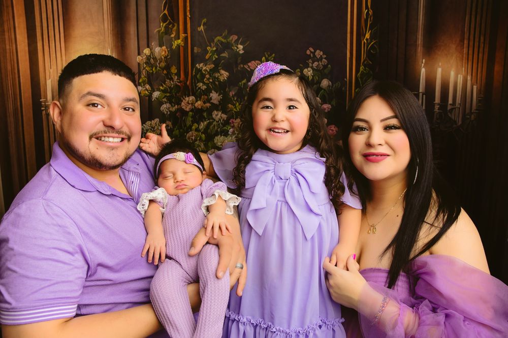 Family portrait with matching purple outfits against dark elegant backdrop.