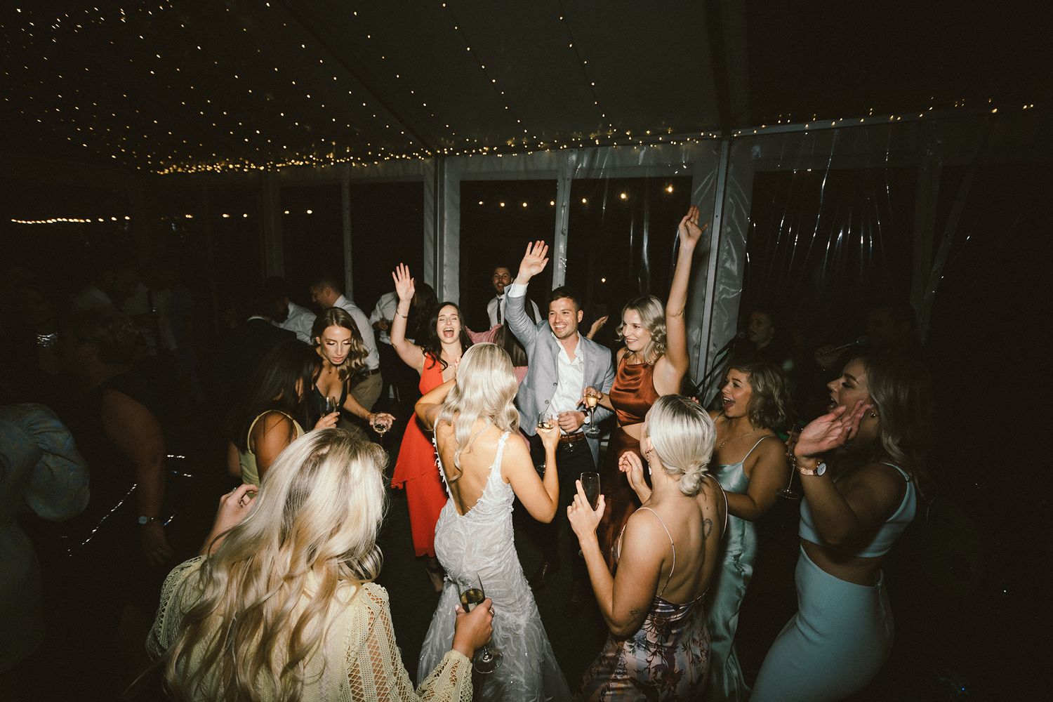 Crowded dance floor at a wedding reception with guests dancing under ambient lighting.