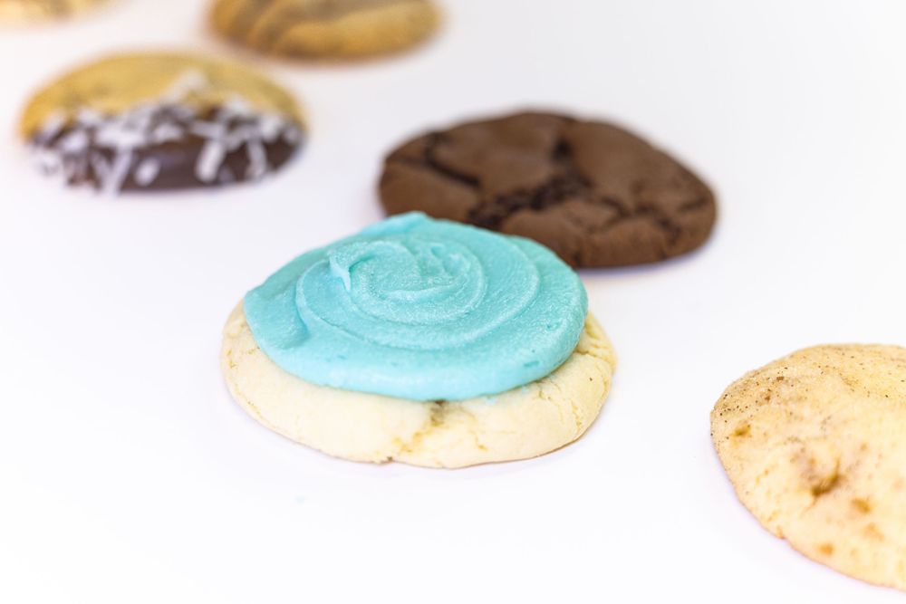 Assorted cookies including one with bright blue frosting on white background.