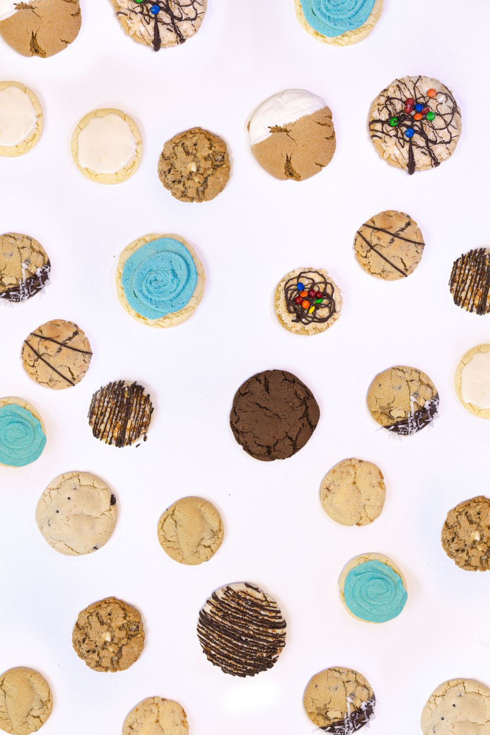 Assorted decorated cookies including chocolate chip, blue frosted, and drizzled varieties arranged on white background.
