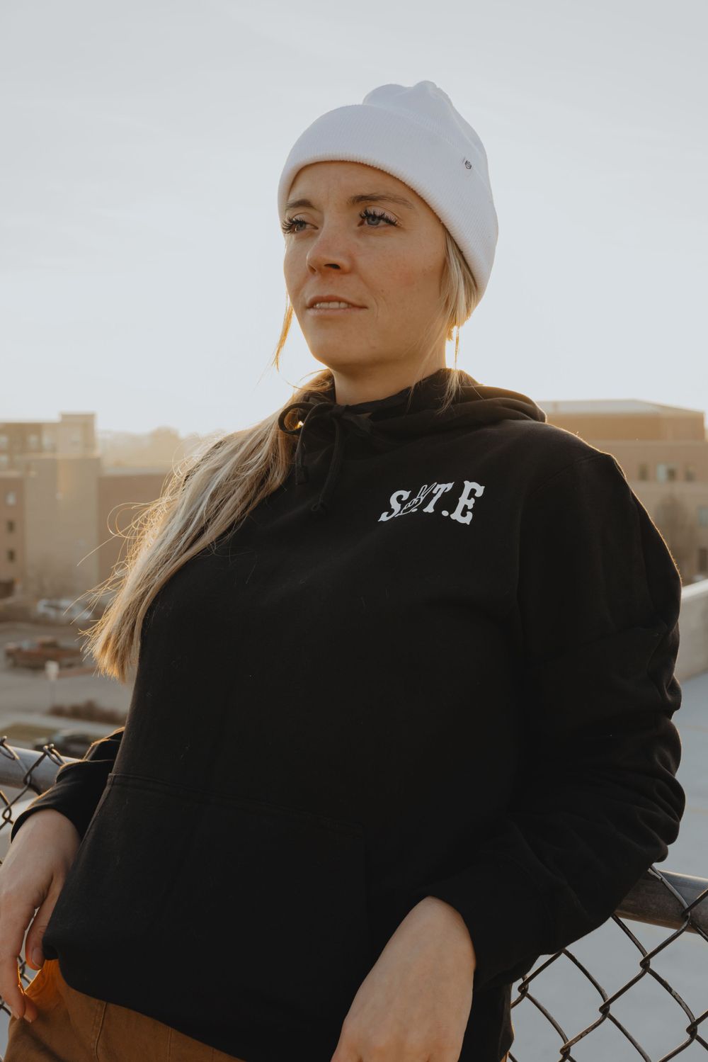 Portrait style photo of someone wearing a white beanie and black hoodie against a sunset backdrop.