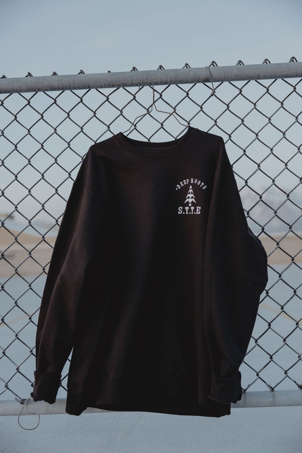 Black long sleeve shirt with STTE logo hanging on chain link fence.