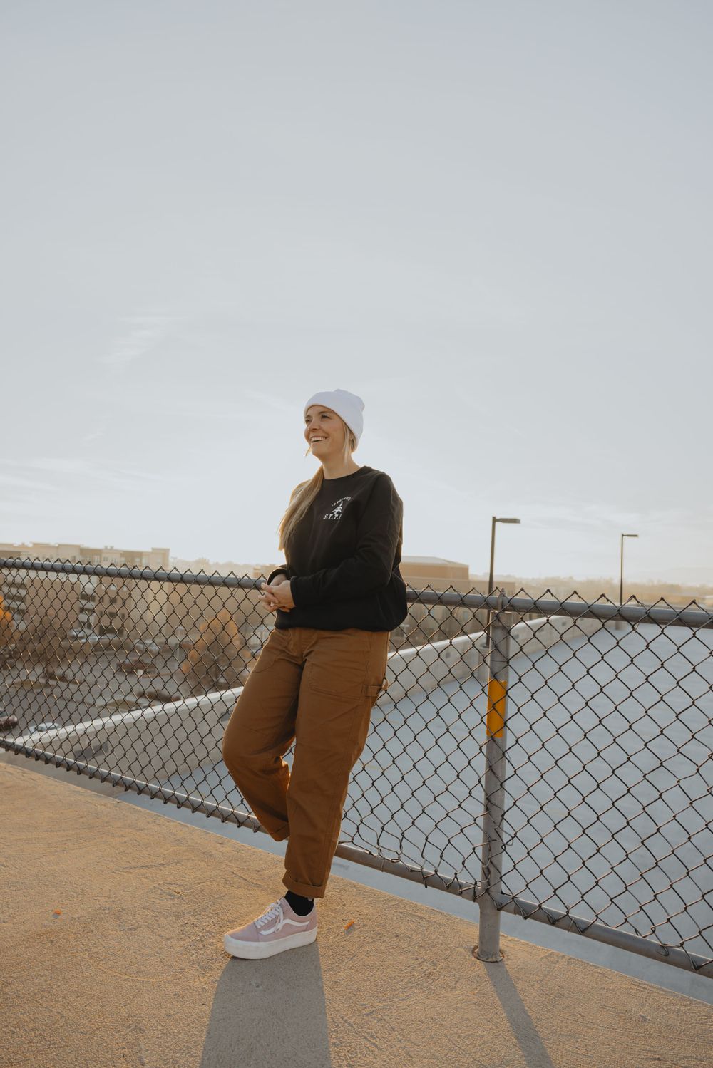 Person in casual wear leaning against chain link fence on an elevated platform.