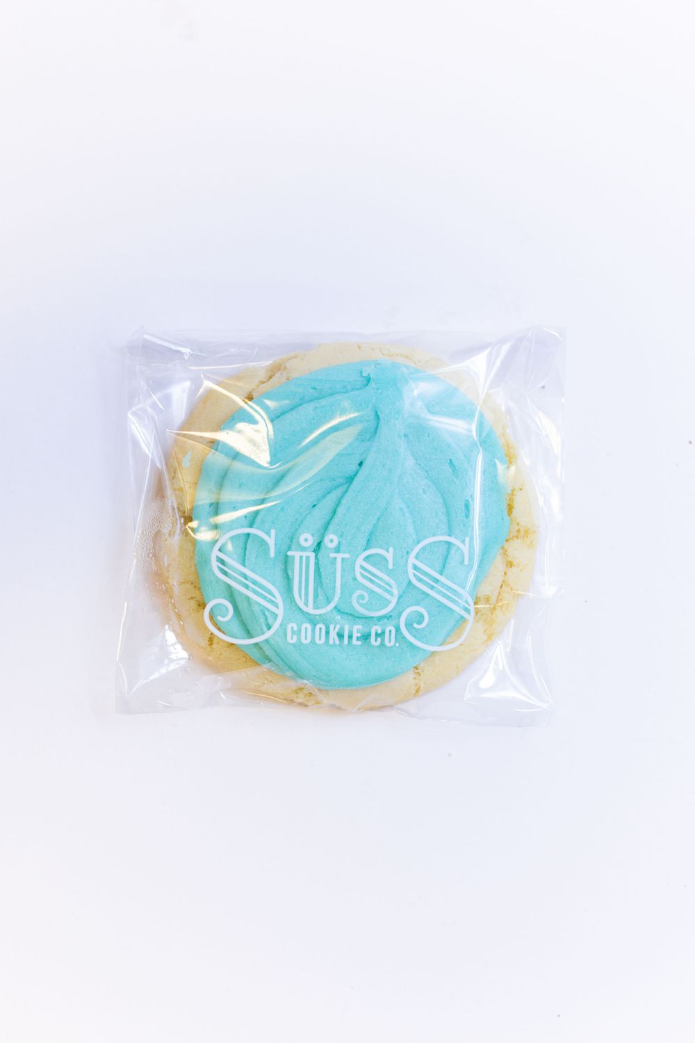 A sugar cookie with turquoise frosting sealed in clear packaging with Suss branding.